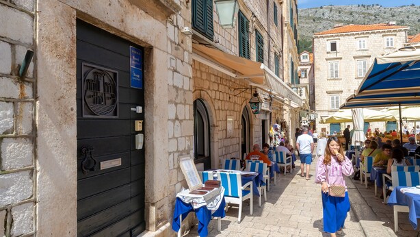 Une rue bordée de terrasses, avec des bâtiments en pierre et un ciel dégagé.