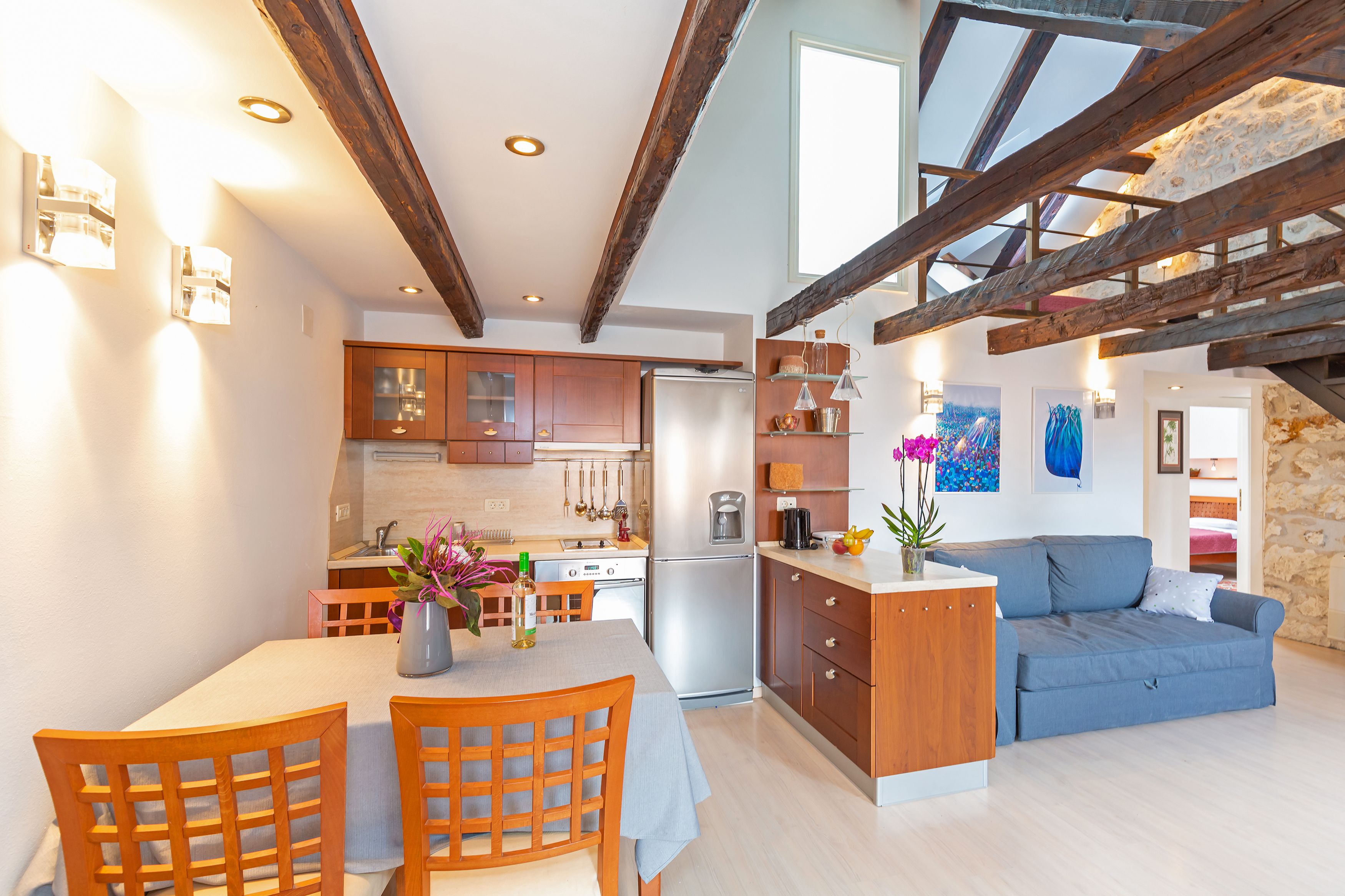 Een moderne keuken met houten kasten, een eettafel met stoelen en een blauwe bank in een ruime woonkamer.