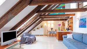 Un appartement moderne de style « loft », avec des poutres apparentes en bois, un téléviseur à écran plat, un canapé, un coin repas et une cuisine.