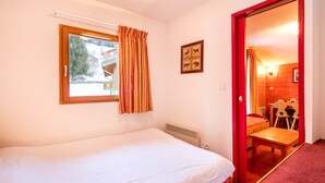 A bedroom with a single bed, a window with curtains, a framed picture on the wall, and a red door leading to a dining area. - Proche du Centre! Appart sympa, Piscine + Sauna (Valfréjus)