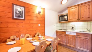 A wooden-paneled kitchen with a dining table set for breakfast, including plates, a glass of orange juice, and pastries. - Proche du Centre! Appart sympa, Piscine + Sauna (Valfréjus)