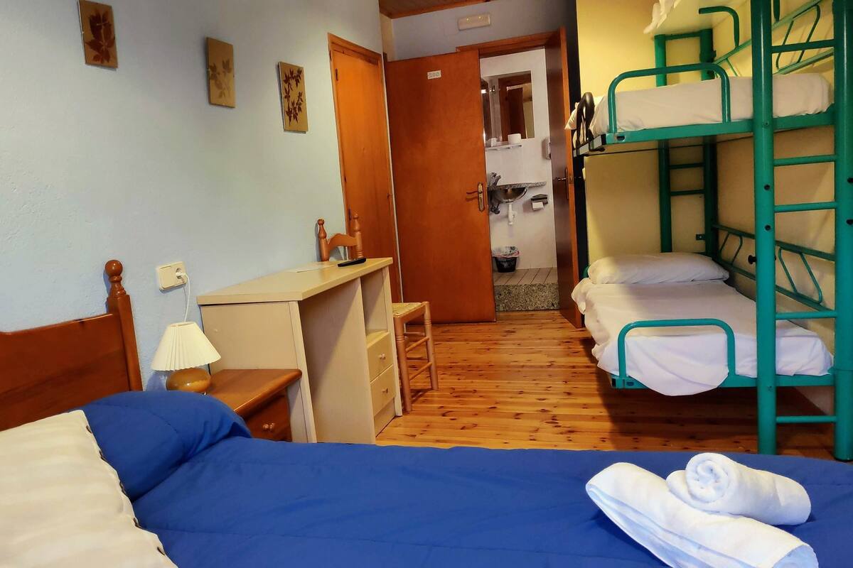 Un dormitorio con literas, escritorio, silla y una pequeña cocina.