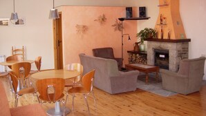 A living room with a fireplace, wooden furniture, and a dining area. - Hostal Pas de la Pera (Lles)