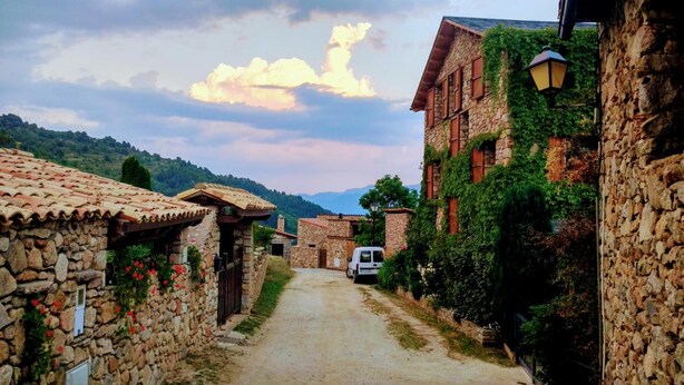A narrow stone pathway leading through a rustic village with traditional stone buildings, some with ivy, and a white van parked on the side. - Hostal Pas de la Pera (Lles)