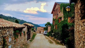 A narrow stone pathway leading through a rustic village with traditional stone buildings, some with ivy, and a white van parked on the side. - Hostal Pas de la Pera (Lles)