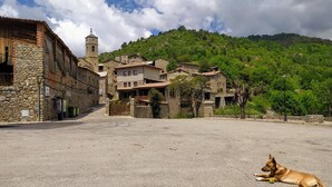 A rural village with stone buildings, a church with a bell tower, and a dog lying on the ground. - Hostal Pas de la Pera (Lles)