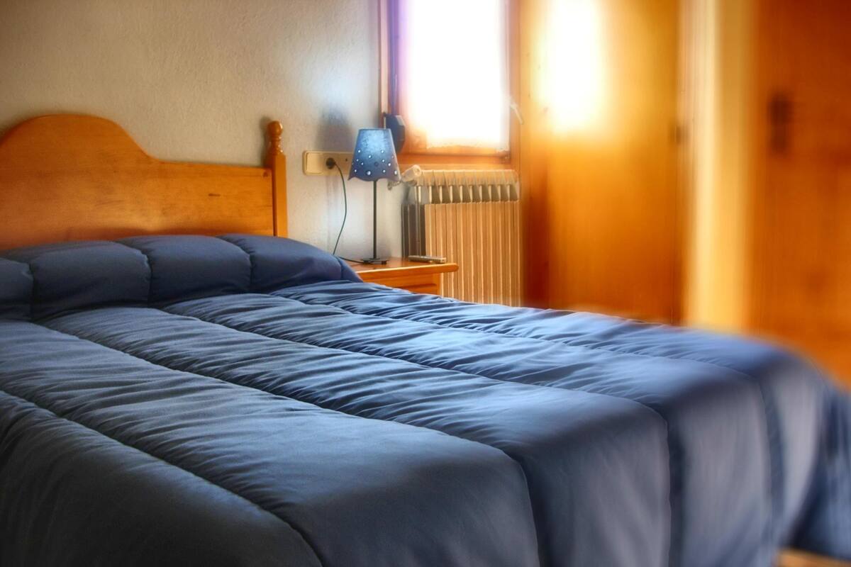 Una cama bien tendida con un edredón azul en una habitación con paredes de madera y una ventana.