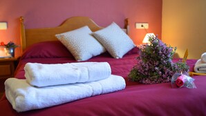 A neatly made bed with a red bedspread, two pillows, and a bouquet of flowers. - Hostal Pas de la Pera (Lles)