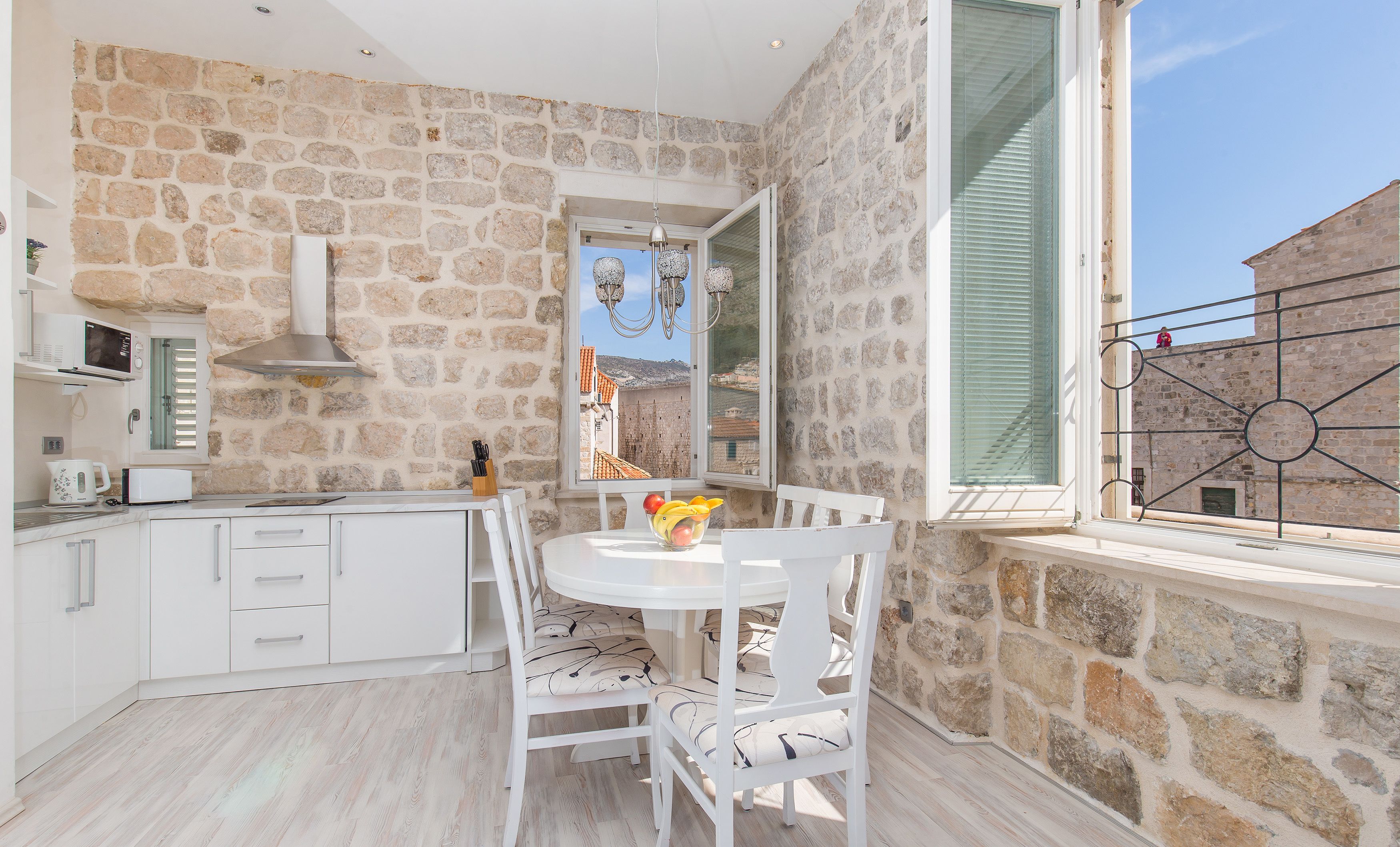 A kitchen with white cabinets, a stone wall, and a window with a view of buildings.