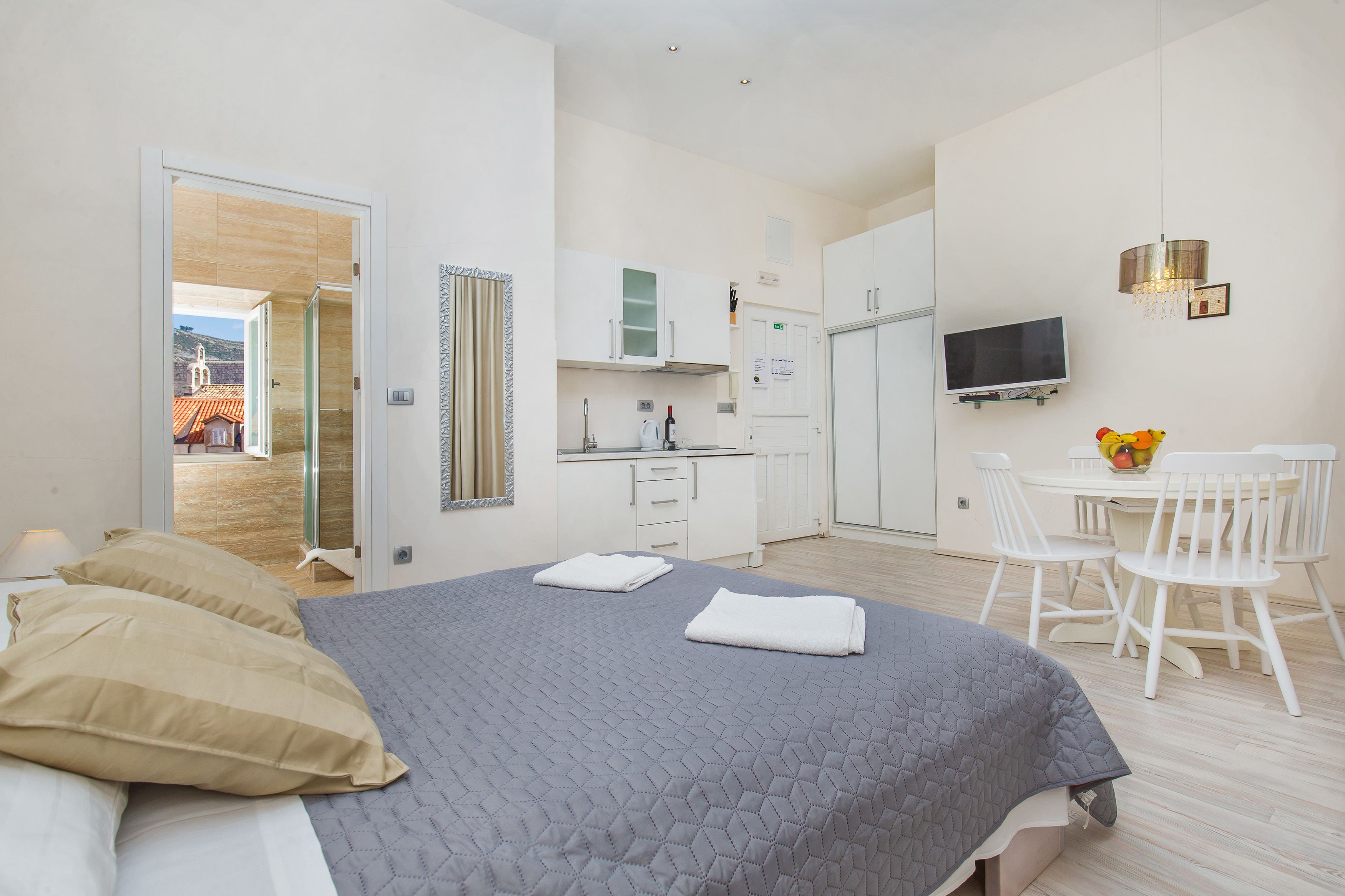 Une chambre avec un lit, une petite kitchenette, un coin repas avec des chaises et un téléviseur fixé au mur.