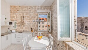 A kitchen with stone walls, a white dining table with chairs, and a view of buildings through a window.