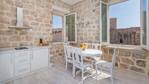A stone-walled room with a white table and chairs, a built-in stove, and a view through a window.