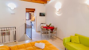 Una habitación luminosa con techo de madera, un comedor con mantel rojo, un sofá verde y un televisor montado en la pared.