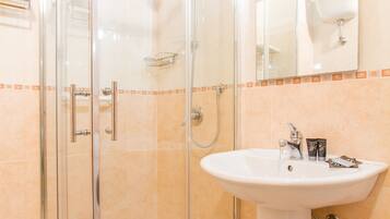 A bathroom with a glass shower enclosure, a white sink, and a mirror above the sink.
