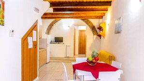 Un comedor con una mesa dispuesta para dos personas, un mantel rojo y un frutero sobre la mesa.