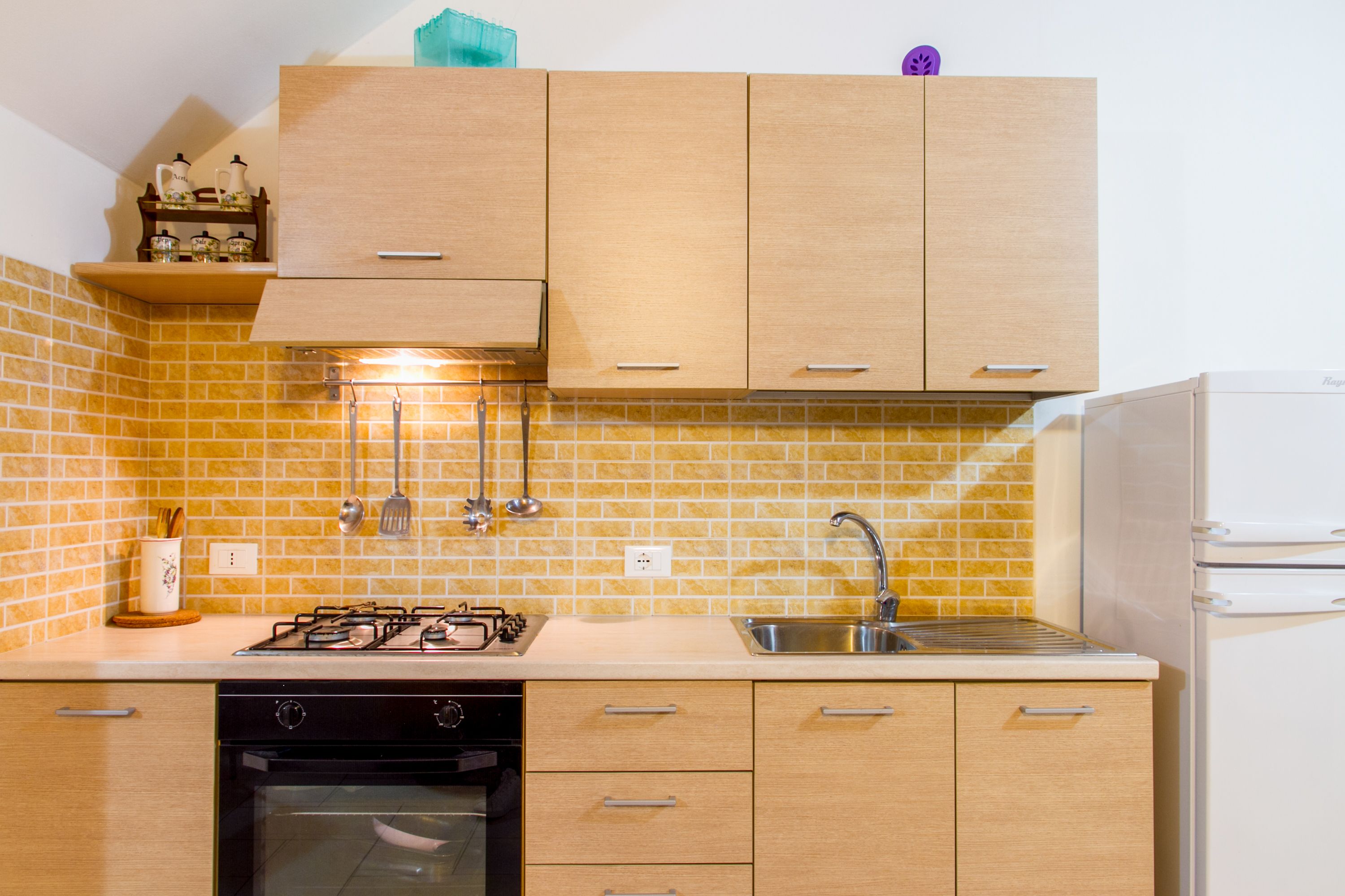 Een kleine keuken met houten kastjes, een gasfornuis, een vaatwasser en een spoelbak.
