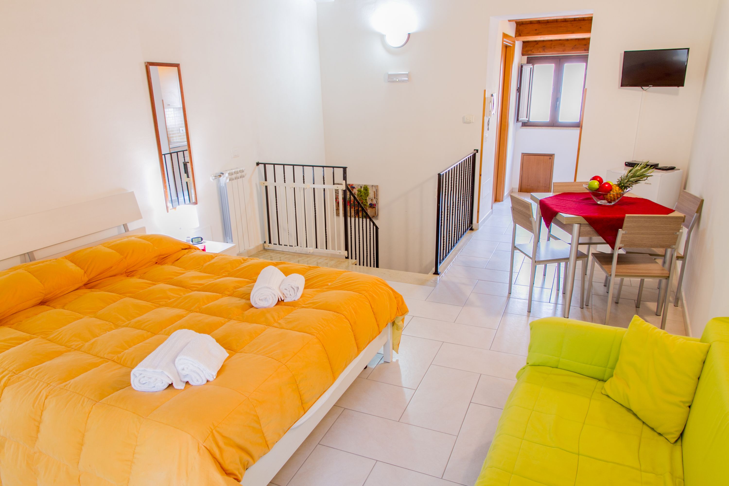 Ein Hotelzimmer mit einem großen Bett, einem grünen Sofa, einem Esstisch mit Stühlen und einem an der Wand befestigten Fernseher.