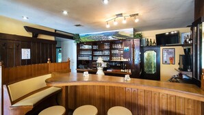 Un espace bar avec des tabourets en bois, un comptoir et des étagères remplies de bouteilles et de verres.
