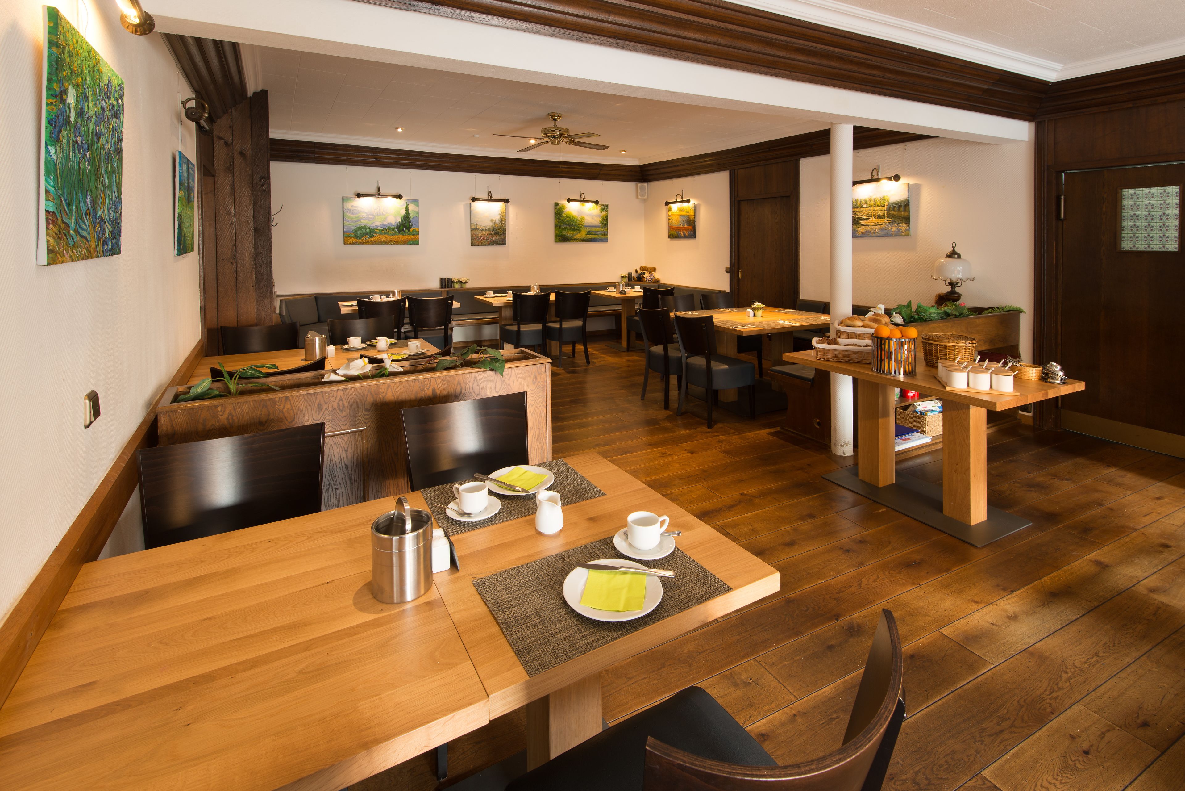 Un restaurant avec des tables et des chaises en bois, un ventilateur de plafond et des lampes fixées au mur.
