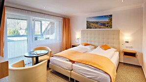 Une chambre d’hôtel avec un lit, une chaise, une petite table, une fenêtre avec des rideaux et un tableau au mur.
