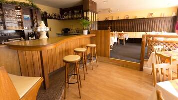 Un espace bar avec des tabourets en bois, un comptoir et un coin salon avec des tables et des chaises.