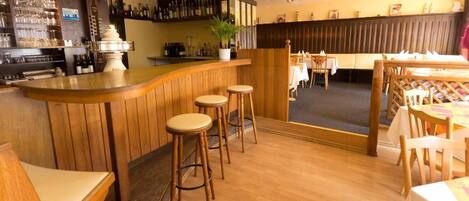 A bar area with wooden stools, a counter, and a seating area with tables and chairs.