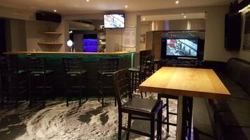 A bar area with a counter, multiple bar stools, a television screen, and a menu board.