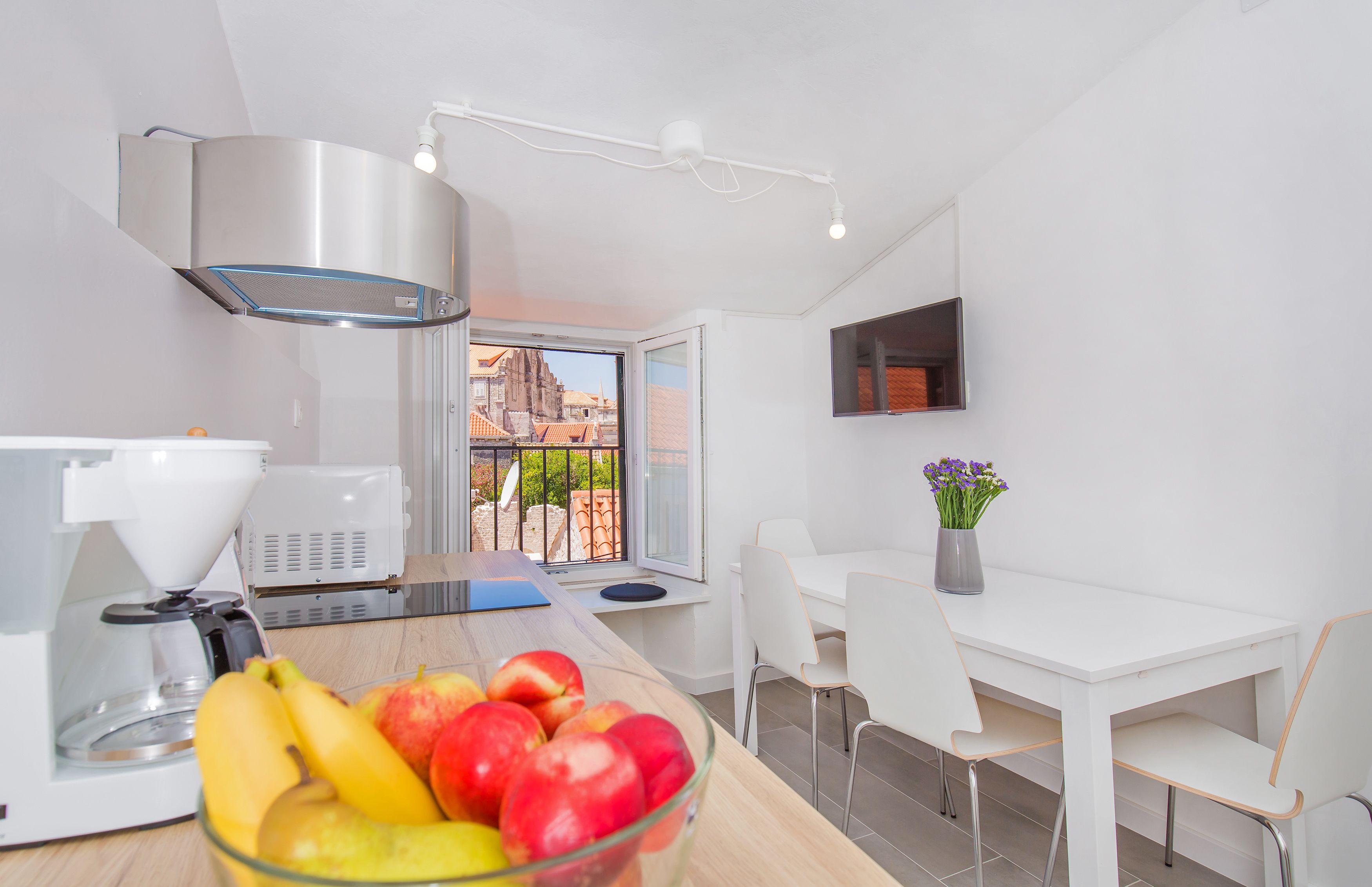 Una cocina moderna con cafetera, un cuenco de fruta y un comedor con mesa y sillas.