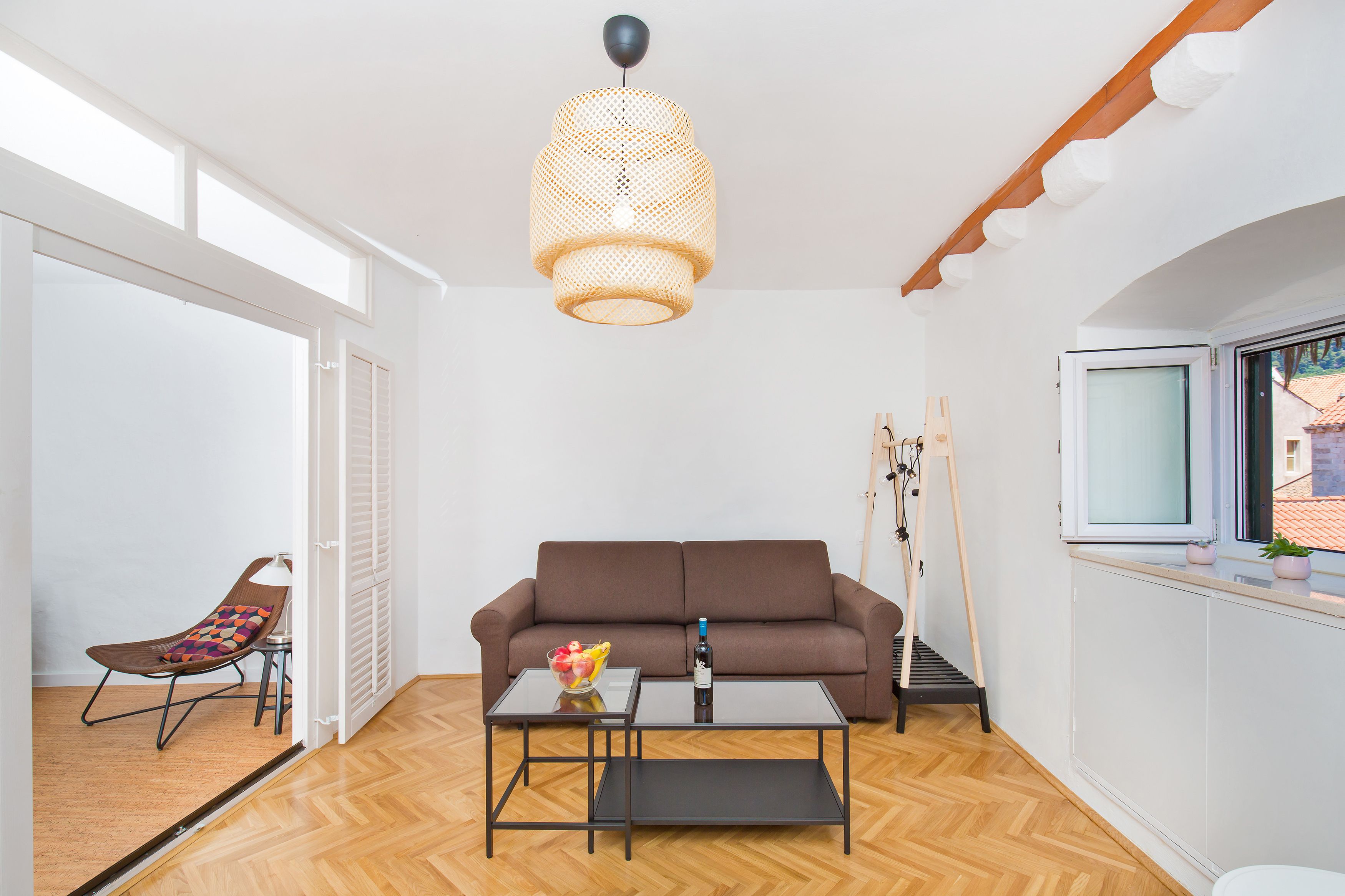 Una sala moderna con un sofá marrón, una mesa de centro de cristal y una lámpara colgante de mimbre.