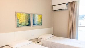 Habitación de hotel con dos camas, una mesita de noche, un teléfono y dos cuadros abstractos en la pared.