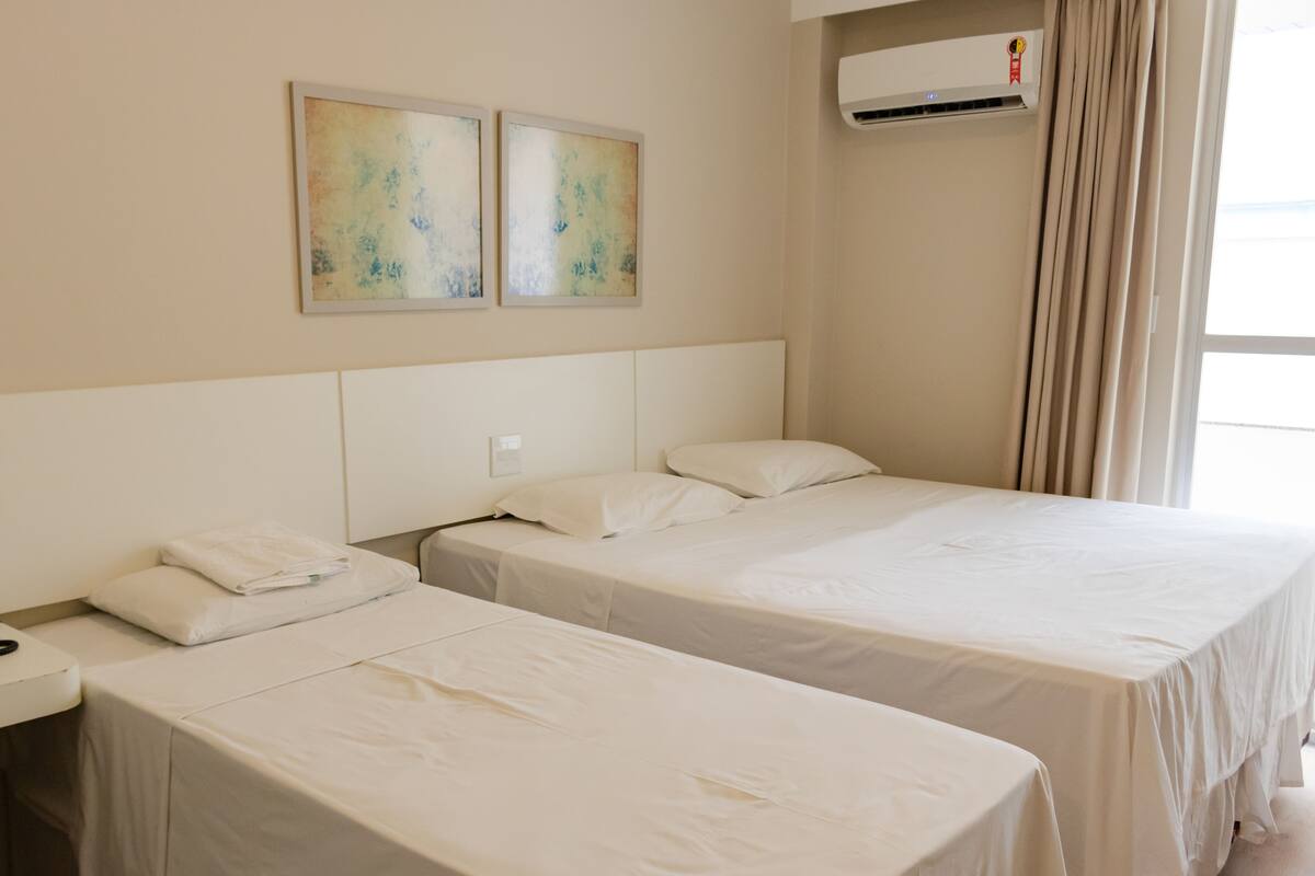Ein Hotelzimmer mit zwei Einzelbetten, einem Nachttisch, einer Wand-Klimaanlage und zwei abstrakten Gemälden.