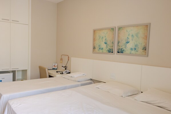 Une chambre d’hôtel avec deux lits simples, un bureau, une chaise et deux tableaux abstraits accrochés au mur.