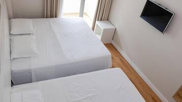 Quarto pequeno e limpo com duas camas, uma televisão de tela plana e uma janela com cortinas.