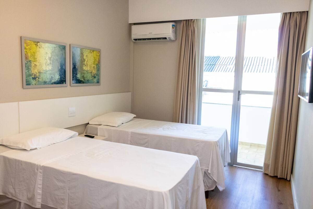 Ein Hotelzimmer mit zwei Einzelbetten, einer Decken-Klimaanlage und einer großen Schiebeglas-Tür, die zu einem Außenbereich führt.