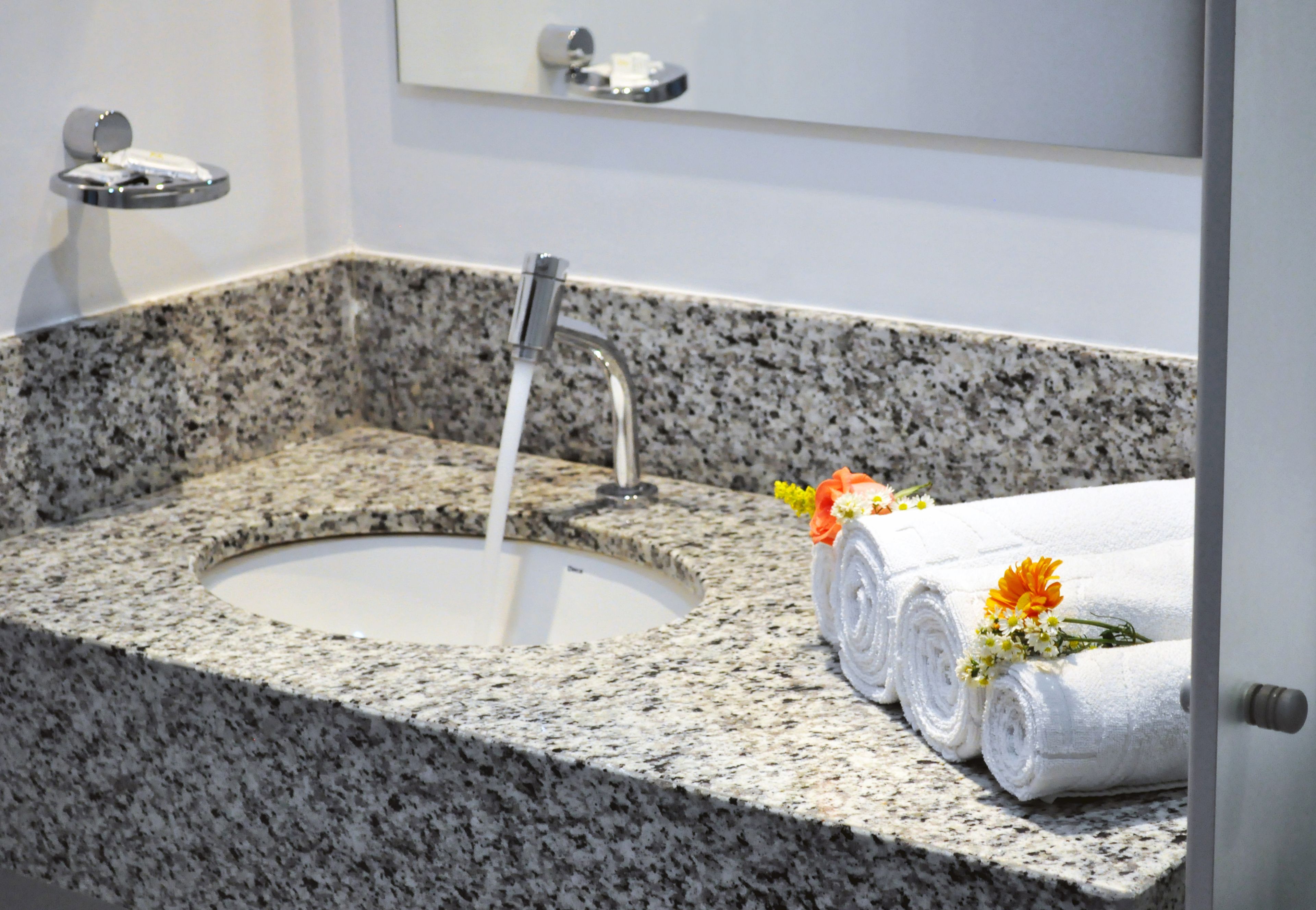 Un lavabo de granito con grifo, un espejo encima y toallas enrolladas con flores a la derecha.
