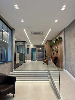 A modern interior with a glass partition, a staircase, and seating areas.