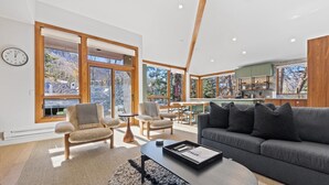 Ein modernes Wohnzimmer mit Sofa, Sesseln, Couchtisch und Essbereich mit Blick ins Freie.