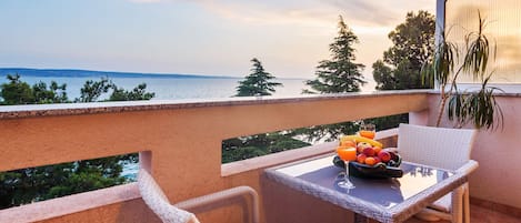 Un balcon avec une table dressée pour le petit-déjeuner, donnant sur un plan d’eau et des arbres.