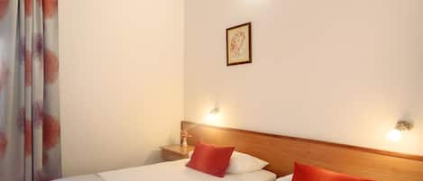 Une chambre d’hôtel avec deux lits, une tête de lit en bois, une table de chevet avec une lampe et un tableau encadré au mur.