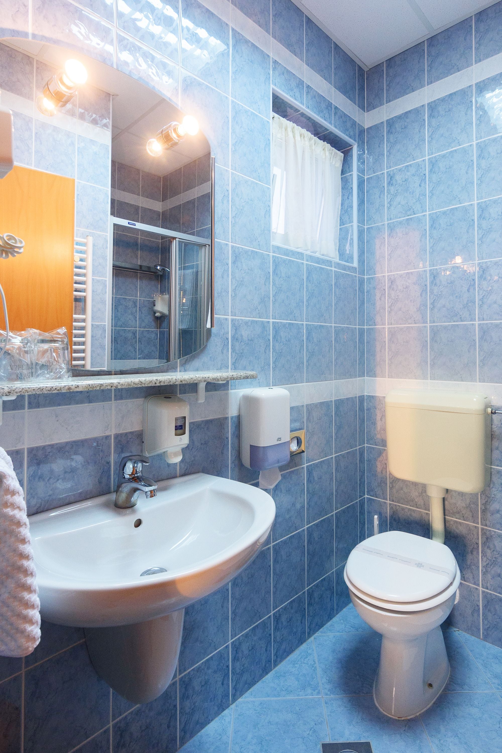 Une salle de bain avec un lavabo, un miroir et des toilettes, le tout adossé à un mur recouvert de carreaux bleus.