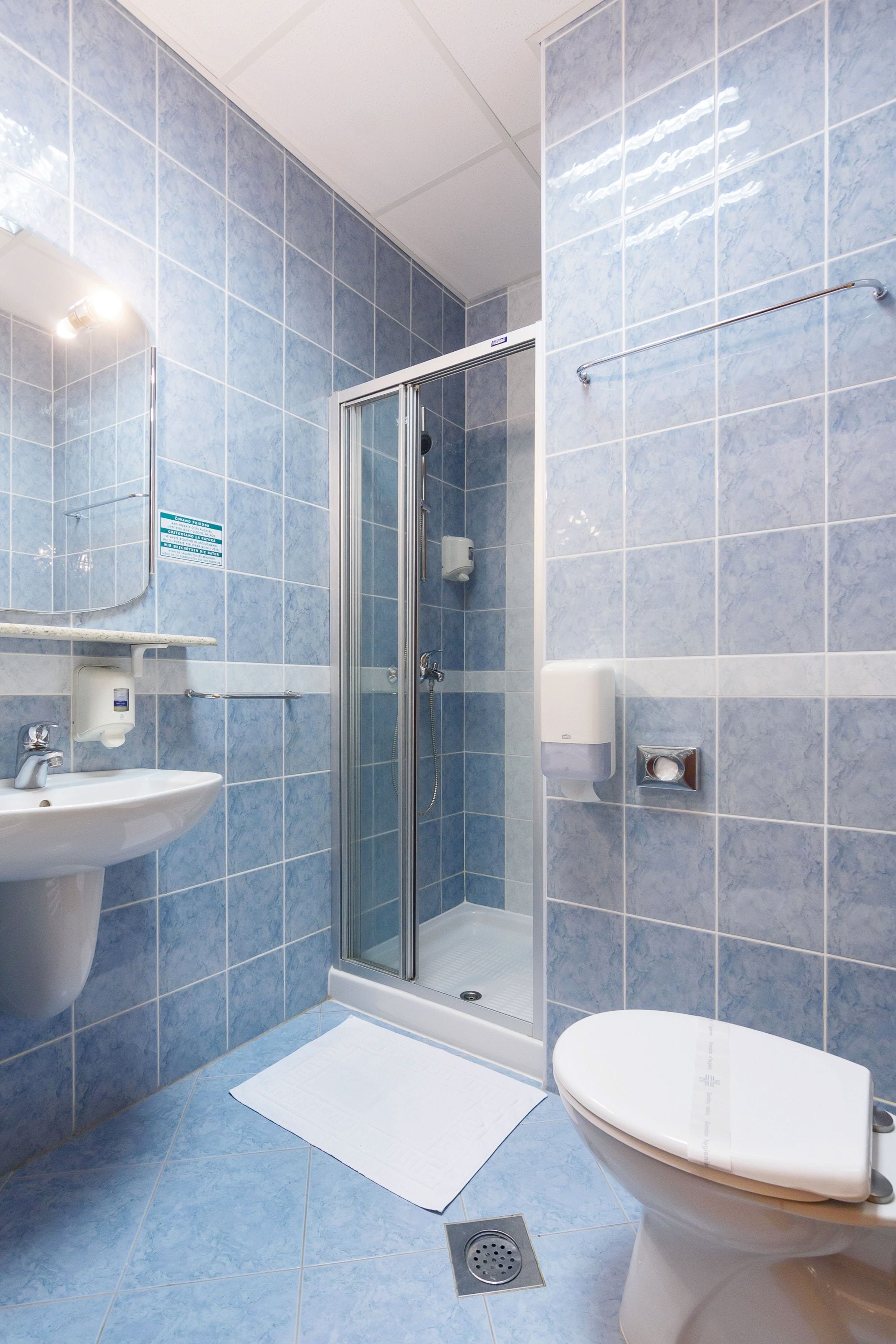 A bathroom with blue tiles, a glass shower enclosure, a white sink, and a toilet.