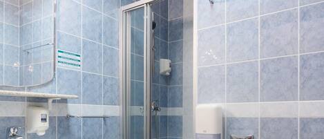 A bathroom with blue tiles, a glass shower enclosure, a white sink, and a toilet.