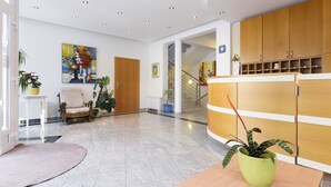 A modern reception area with a wooden reception desk, potted plants, a staircase, and a painting on the wall. - Villa Vicko (Starigrad)