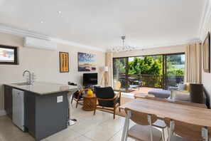 Relax in this well-appointed living space with a central island, comfortable seating area, and large windows offering a view of lush greenery.