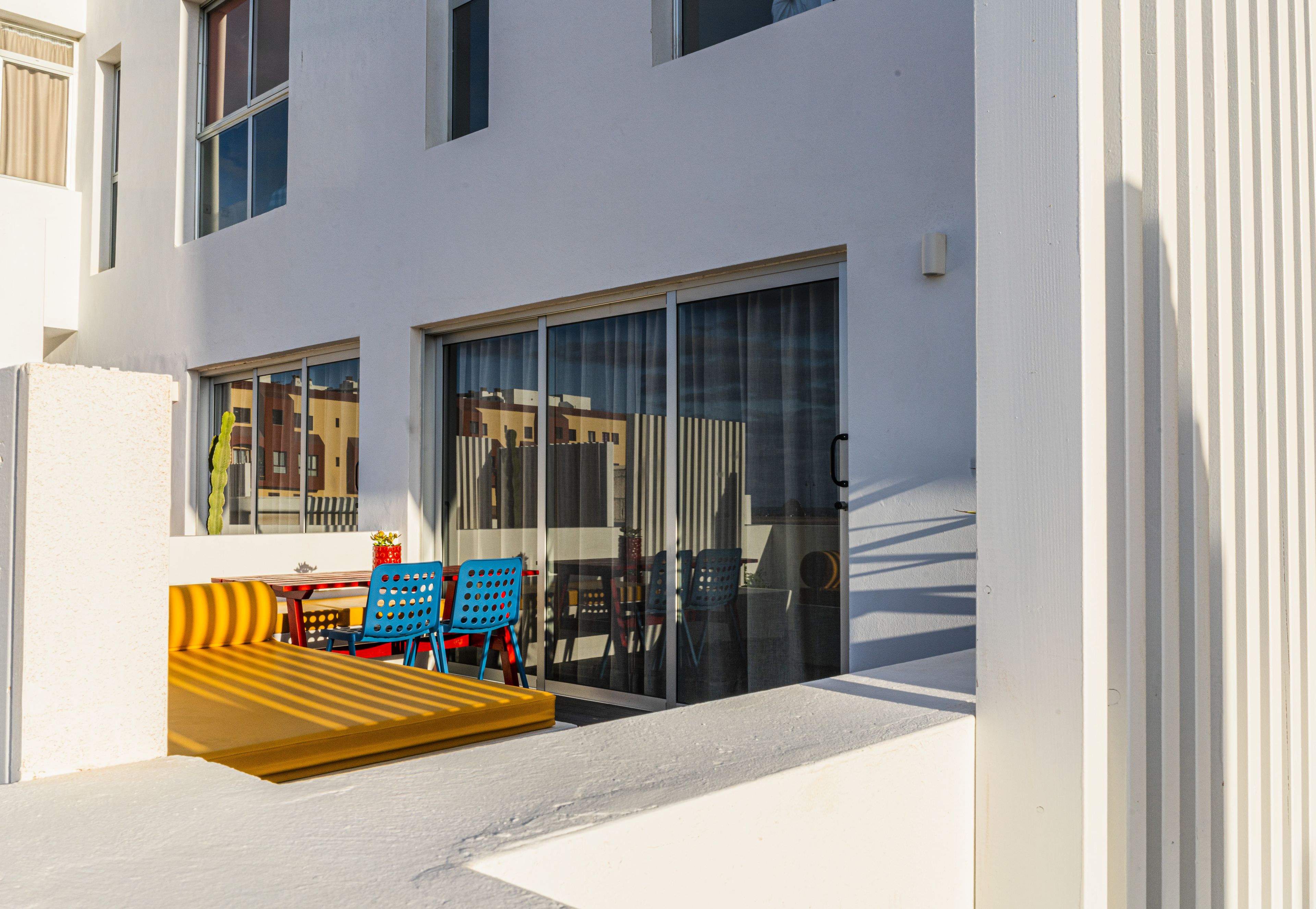 Un edificio moderno con puerta de vidrio, rampa amarilla y sillas de colores en el exterior.