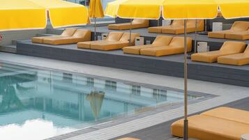 Un área junto a la piscina con sombrillas amarillas y sillones reclinables color beige.