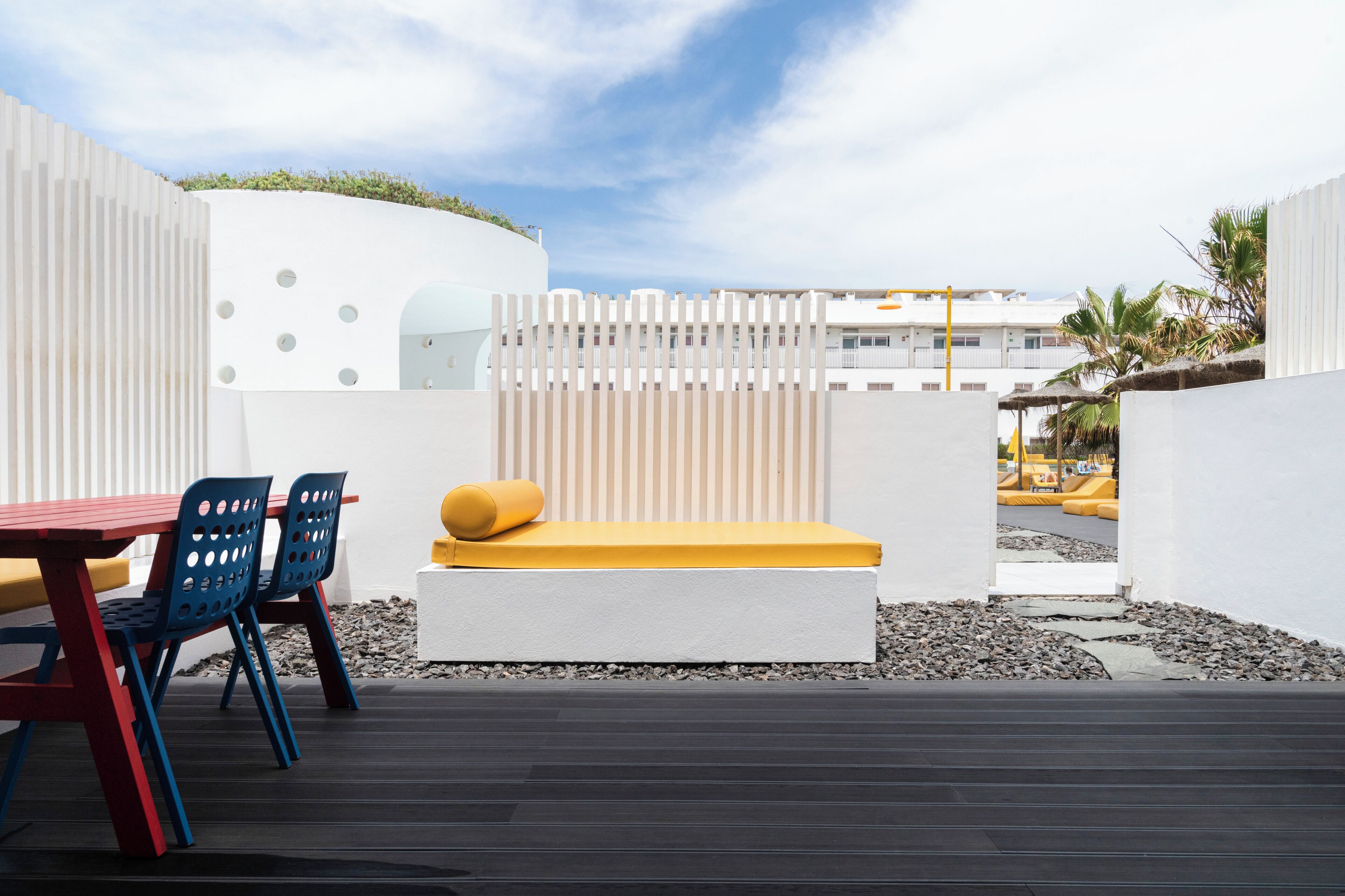 A modern outdoor seating area with a white bench, blue chairs, and a red table.