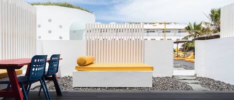 A modern outdoor seating area with a white bench, blue chairs, and a red table.