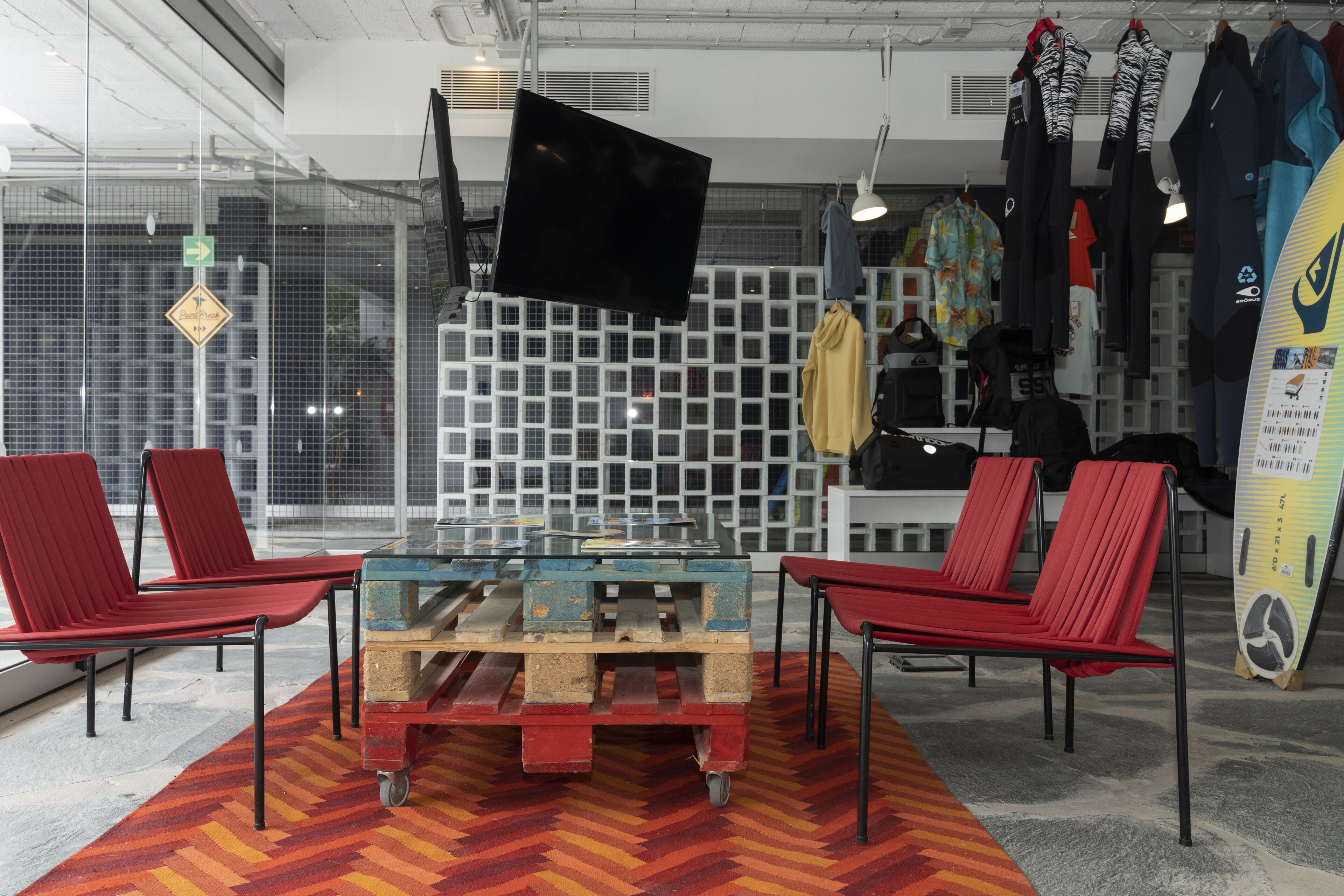 Une pièce moderne avec une table en verre entourée de chaises rouges, un téléviseur fixé au mur et des planches de surf accrochées au mur.