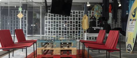Une pièce moderne avec une table en verre entourée de chaises rouges, un téléviseur fixé au mur et des planches de surf accrochées au mur.